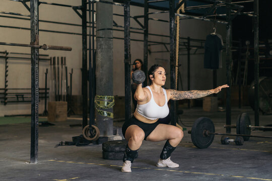 Strong woman exercising in a gym with weights and dumbbells.