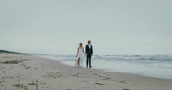 The bride and groom run away from the wave walking along the seashore