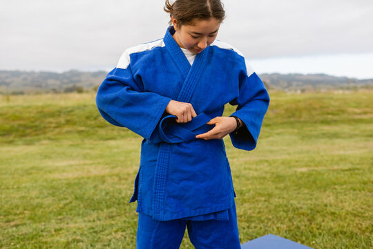 Judoka girl fastening blue belt outdoor
