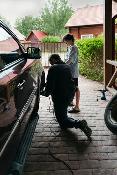 Teenager helps father repair car.