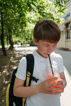 Young schoolboy with backpack drinks lemonade outdoor.