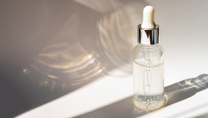 A white transparent bottle with serum in the rays of the sun - obrazy, fototapety, plakaty