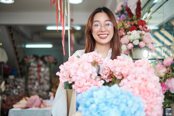 Portrait of young beautiful Asian woman florist with floral bunch delivery, smiling and looking at camera, lovely business entrepreneur, flower shop happy work, brightly colorful flora bouquet store.