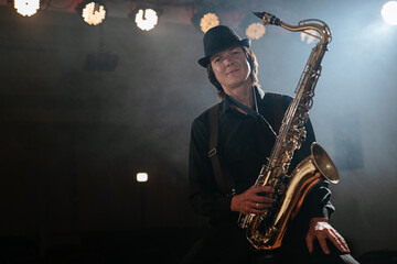 Friendly man sitting on chair with saxophone in his hand and looking at camera
