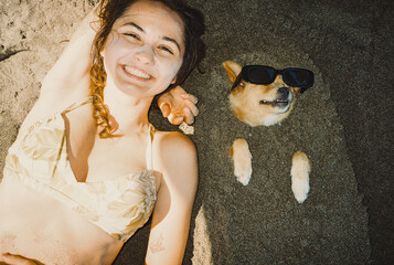 Woman laying near the dog with sunglasses on the beach
