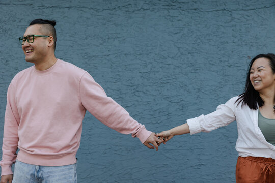 Playful, happy couple having fun holding hands together near blu