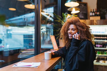 Cheerful black woman talking on smartphone in cafe