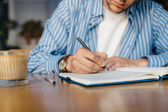 A man writes in a notebook while sitting indoors