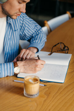 A man writes in a notebook while sitting indoors