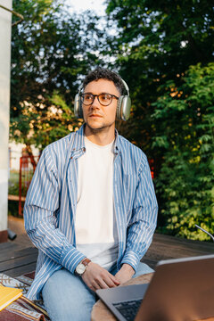 A man with headphones is sitting in front of a laptop outdoors