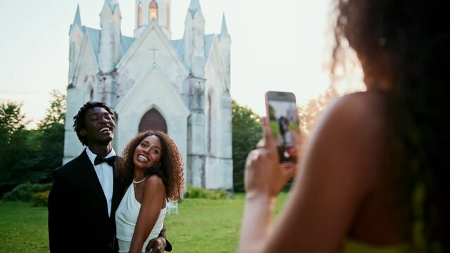 A woman takes pictures of the bride and groom on a mobile phone standing near the church