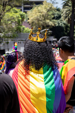 Person With Curly Hair Wearing A Golden Crown And The LGBT+ Flag