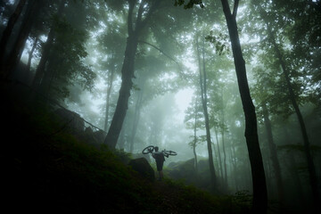 Adventurer carries a bicycle through a foggy forest