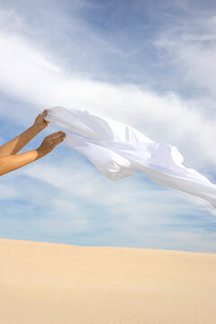 A woman's hands with a fabric against a background of sky and dune.