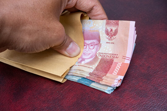 row of Indonesian rupiah banknotes in a salary envelope, on a brown and maroon leather sova