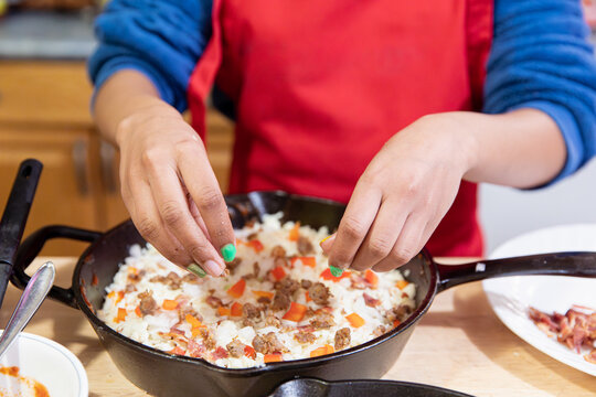 Closeup of a pair of child’s hands sprinkling sausage onto a pizza