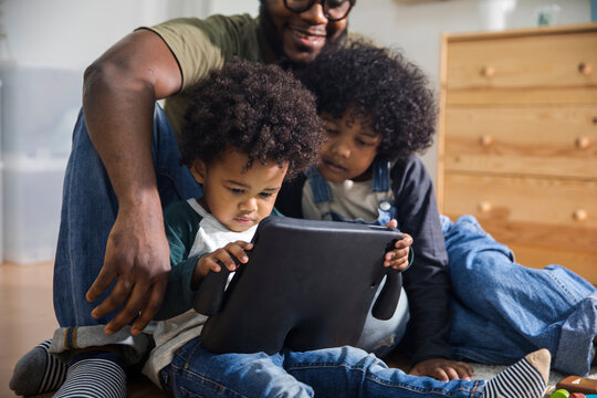 Man spending leisure time with kids using digital tablet at home
