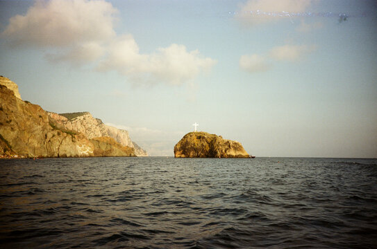 Rocky sea cliff facing sea stack with large white cross on top