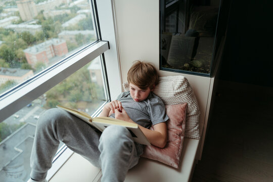 Kid lying on windowsill with book.