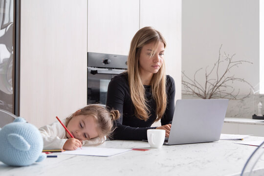 Mother working on netbook near daughter in kitchen