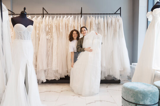 Assistant and client with wedding dress in boutique