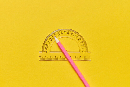 Pink pencil and protractor on bright yellow background.