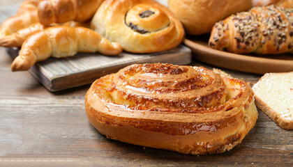 Freshly baked spiral bun and other pastries on wooden table, closeup