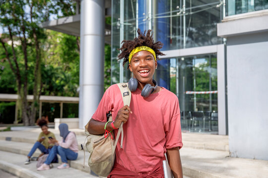 Smart cheerful boy student with bag, headphones and laptop