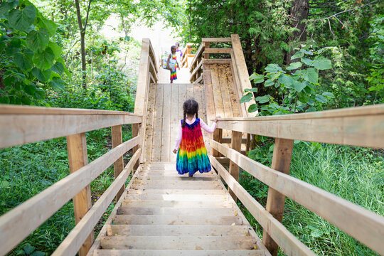 Child in rainbow dress walking down a long flight of wooden stairs