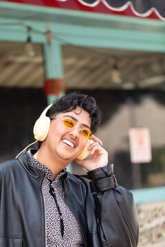 Stylish nonbinary person listening to headphones in cute neighborhood