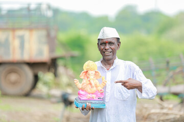 Indian old man holding Lord Ganesha idol in hands , happy old poor man