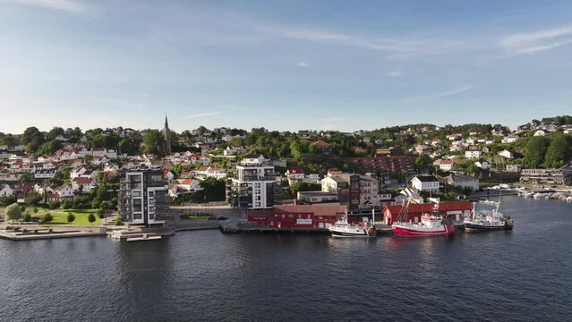 Waterfront Buildings With Moored Boats And Mist On A Sunny Morning In Arendal, Norway. aerial arc shot
