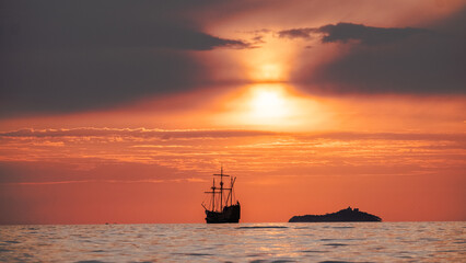 Orange sunset  with
old historical tall ship (yacht) in sea.