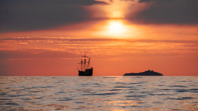 Orange sunset  with
old historical tall ship (yacht) in sea.
