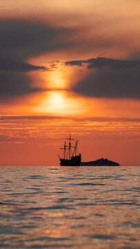 Orange sunset  with
old historical tall ship (yacht) in sea.