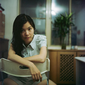 The woman sat in the room with her hands on the back of the chair