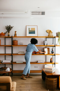 Anonymous afro woman organizing and decorating big shelve 