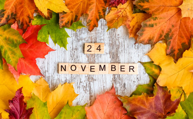 Naklejka na ściany i meble Autumn maple foliage inscription 24 NOVEMBER in wooden letters on the table autumn background