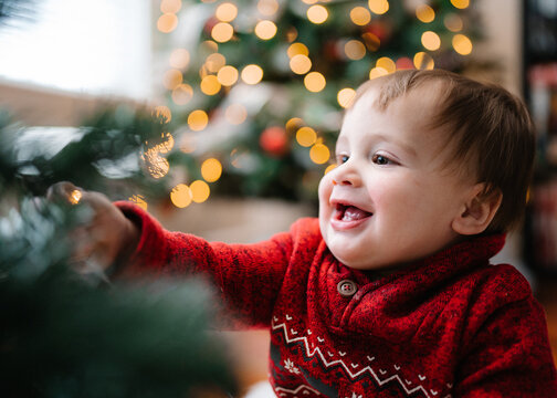 Happy baby decorates a Christmas tree with string lights