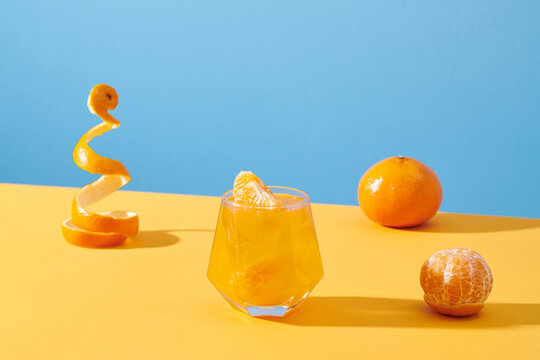 tangerines cocktail with ice on yellow table over blue background