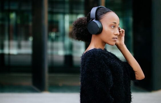 Black Woman In Headphones Standing Near City Building