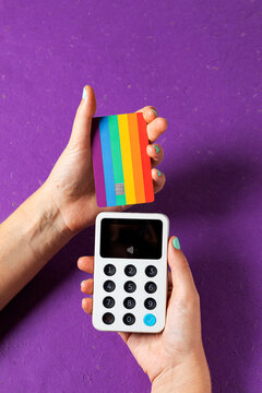 Hands holding a credit card  with LGBTQ colors and a terminal