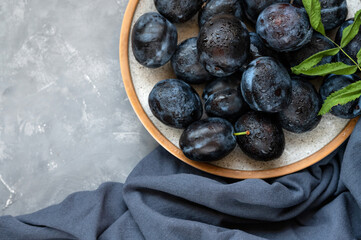 Ripe plum fruits on plate with water drops, on dark blue tablecloth and gray background. Aesthetic flat lay, closeup