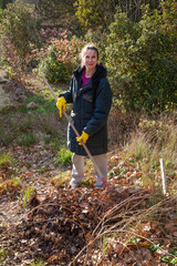 Woman gardening, picking up the fallen autumn leaves with a rake at the beginning of winter, in...