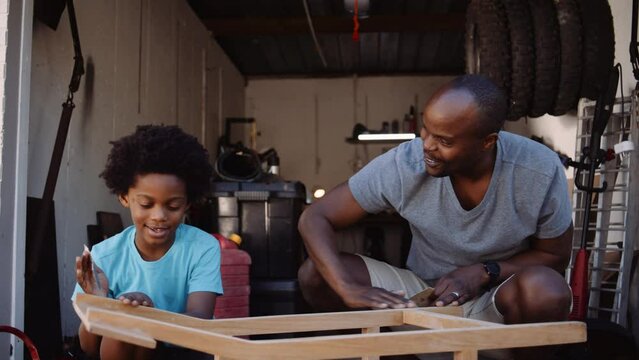 Mixed race father and son sand DIY furniture in home workshop garage 