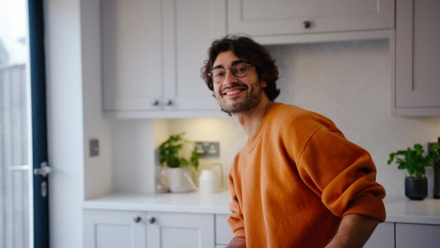 Portrait of smiling young man wearing glasses taking a break with cup of coffee sitting at kitchen counter at home with copy space on left side of frame - shot in slow motion
