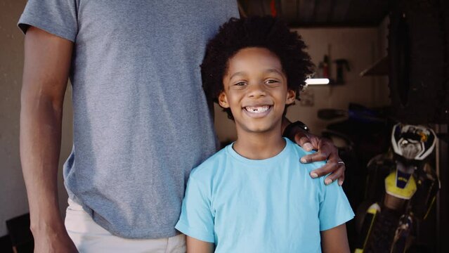 Close up portrait of father and son smiling at camera in their home bike workshop in garage