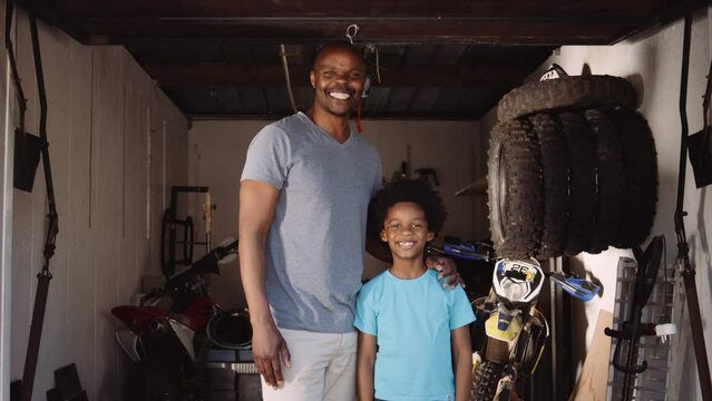 Wide portrait of father and son smiling at camera in their home bike workshop in garage