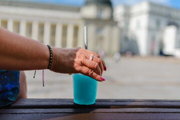 A woman holds a refreshing blue slushy in her hand at the summer city.