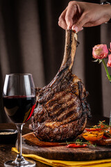 The chef holds a large piece of roasted meat on the bone, tomahawk, lamb or veal.